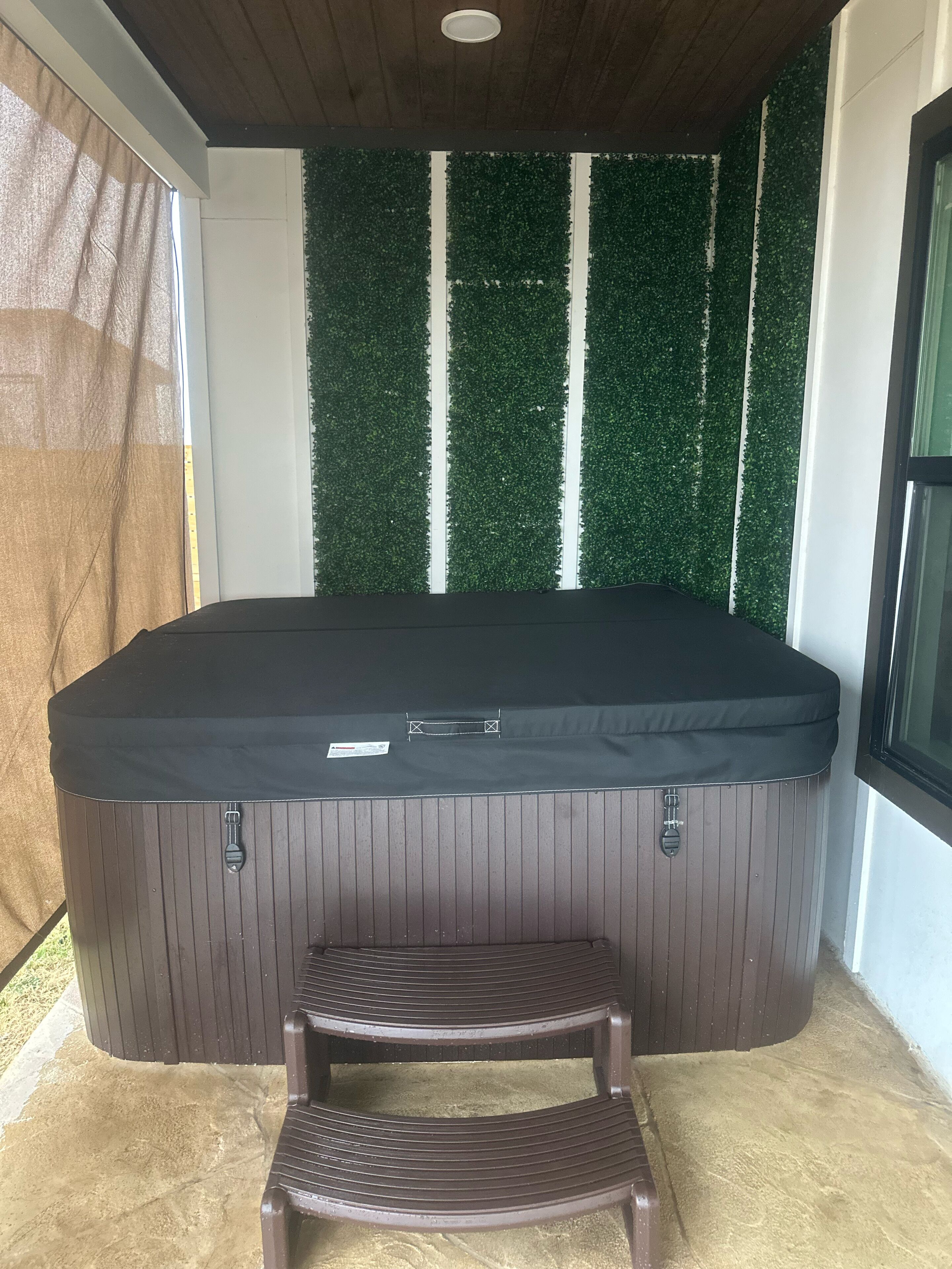A hot tub with a wooden bench in front, surrounded by a wall with green artificial grass and white stripes.