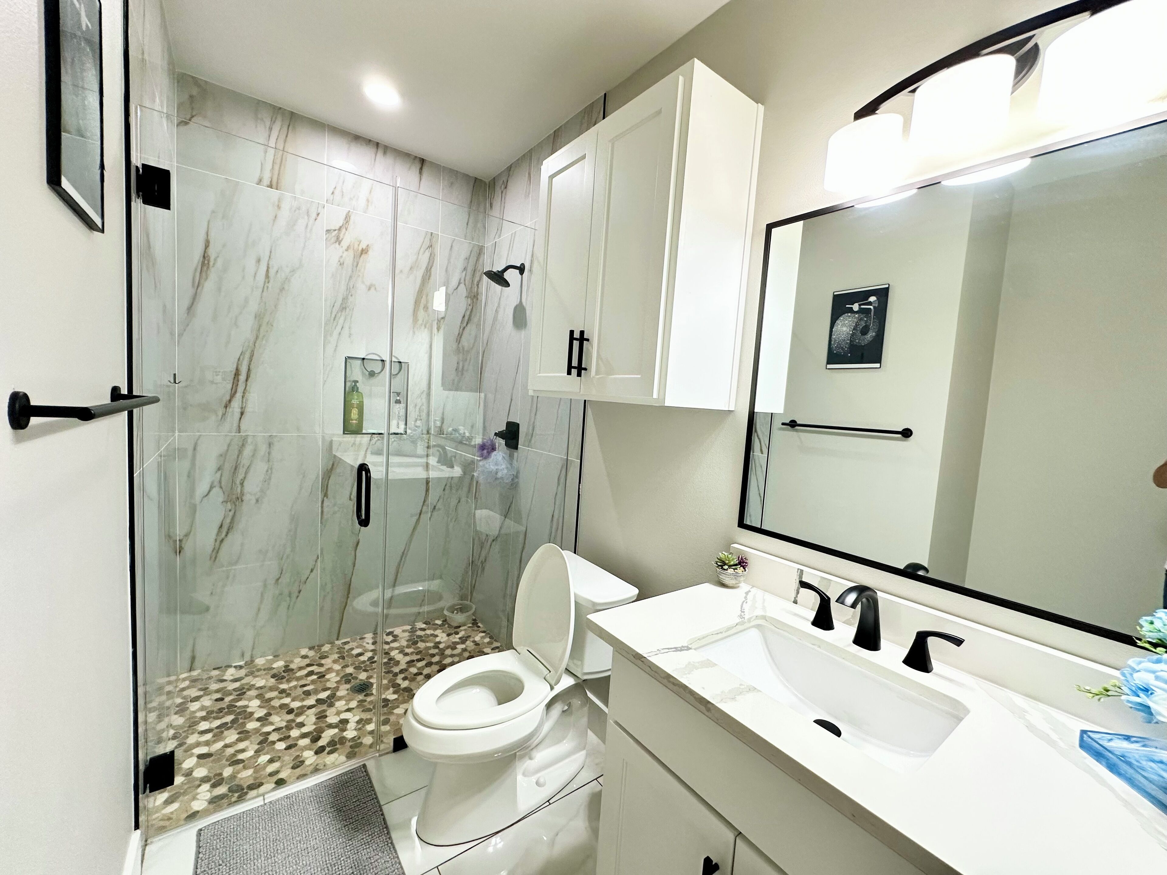 Un bany modern amb dutxa envidrada amb vidre, vàter blanc i un lavabo amb rentapel orells i mirall.