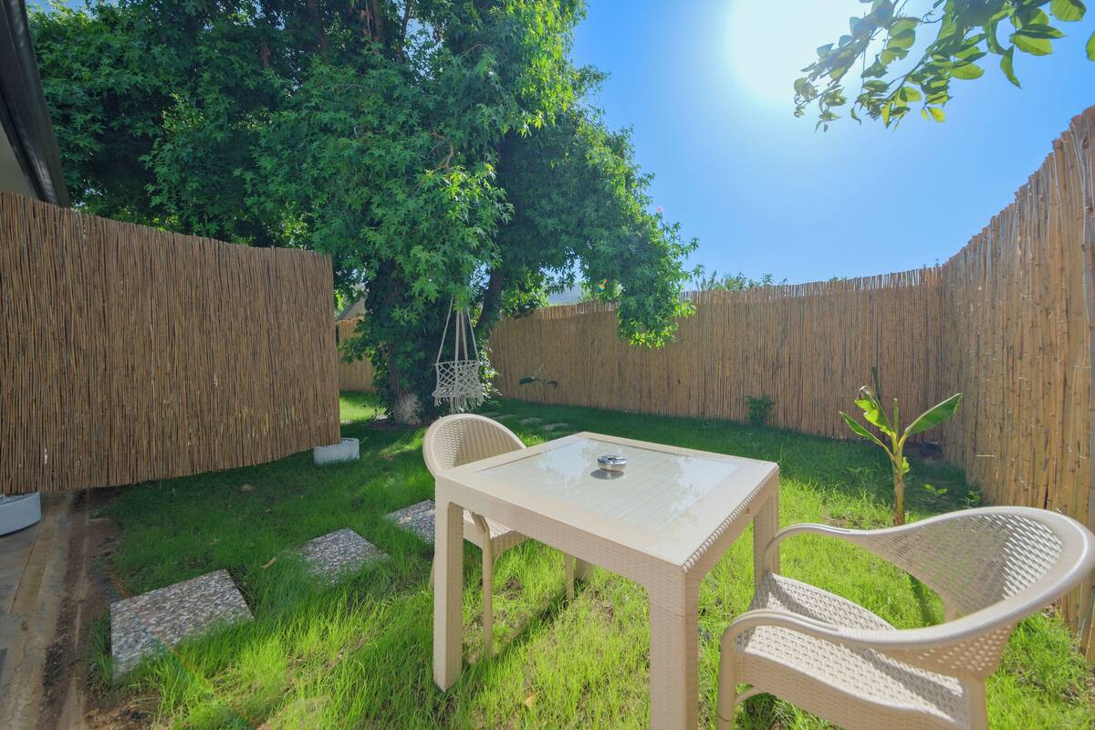 A backyard with a table and two chairs, surrounded by a wooden fence and greenery.