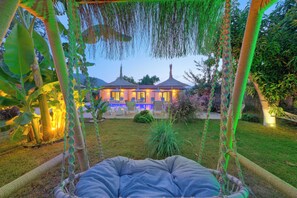 A hammock in a garden with a pool and umbrellas in the background. - Kayaköy Suite  (Fethiye)