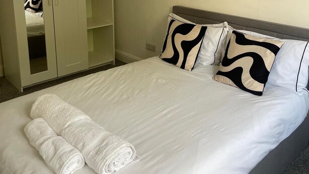 A neatly made bed with white linens and two pillows with a black and white pattern. - Privategarden- Freeparking- wd- 2br- Wifi (Glasgow)