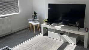 A modern living room with a large flat-screen TV, a small round table with chairs, a radiator, and a potted plant. - Privategarden- Freeparking- wd- 2br- Wifi (Glasgow)