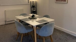A dining area with a white table, four grey chairs, a black floor lamp, and a framed picture on the wall. - Privategarden- Freeparking- wd- 2br- Wifi (Glasgow)