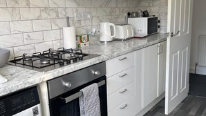A modern kitchen with a gas stove, oven, and dishwasher. There are white cabinets, a marble backsplash, and a microwave on the countertop. - Privategarden- Freeparking- wd- 2br- Wifi (Glasgow)