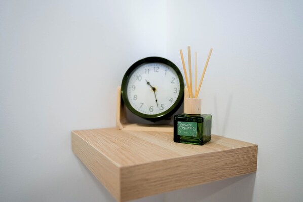A wooden shelf with a clock and a bottle of scented oil.