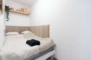 Una cama bien hecha con un cabecero color crema, una pared blanca y un estante de madera encima.