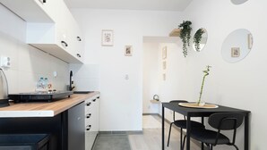 A modern kitchen with a wooden countertop, black chairs, and a dining table. There are framed pictures on the wall and a hanging plant. - A2 Vistula Apartments Kraków (Kraków)