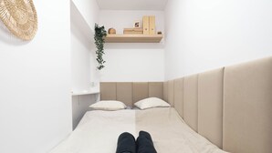 A minimalist bedroom with a single bed, two pillows, a headboard, a shelf with a plant, and a woven basket. - A2 Vistula Apartments Kraków (Kraków)
