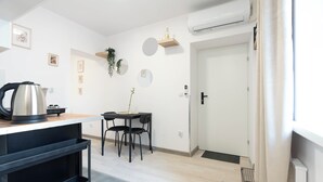 A modern kitchen with a kettle, a small dining table, and chairs. There is a white door with a black handle, and an air conditioning unit mounted on the wall. - A2 Vistula Apartments Kraków (Kraków)