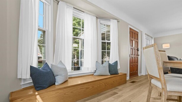 Een kamer met een houten bank bij een groot raam, een houten stoel en een deur.