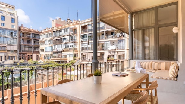 A balcony with a wooden table and chairs, a sofa, and a potted plant. - Apartamento de Tres Habitaciones con Terraza 11B (Barcelona)