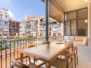 A balcony with a wooden table and chairs, a sofa, and a potted plant. - Apartamento de Tres Habitaciones con Terraza 11B (Barcelona)
