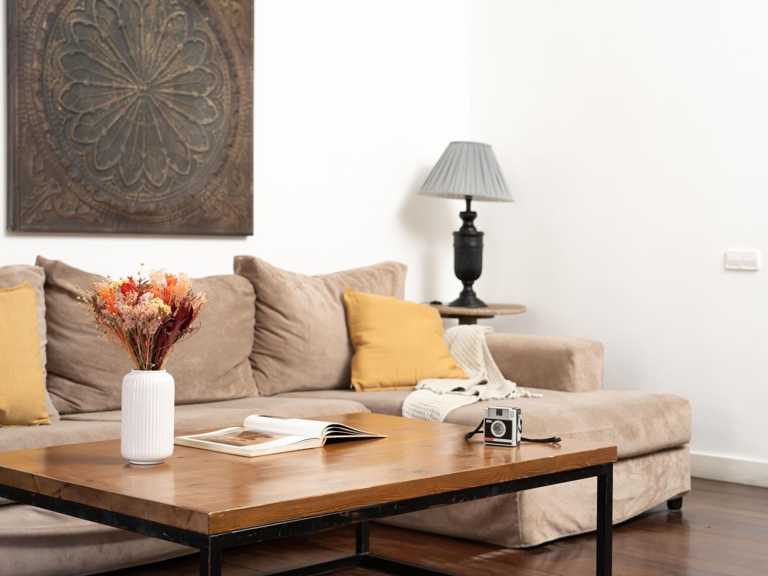 A living room with a sofa, a coffee table, a lamp, and a decorative vase with flowers.