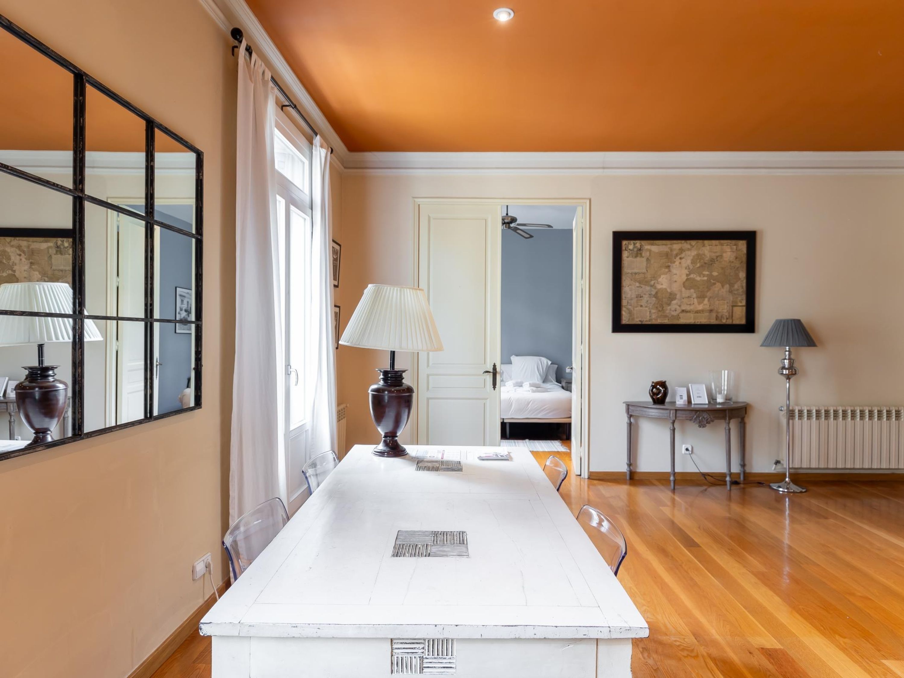 Habitación de hotel con un espejo grande, una mesa blanca, una cama y un radiador.