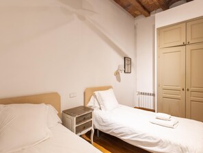 Une chambre avec deux lits, une table de chevet, une lampe fixée au mur et un radiateur.