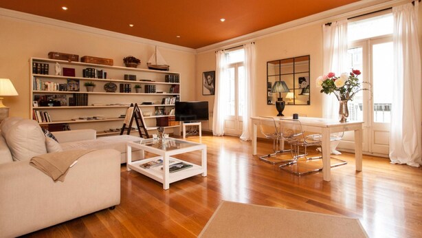 A spacious living room with a white sofa, a coffee table, a bookshelf, a TV, and a dining area with chairs. - Apartamento de dos Habitaciones (Barcelona)