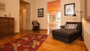 A cozy living room with a sofa, a wooden dresser, a red floral rug, and a dining area in the background. - Apartamento de dos Habitaciones (Barcelona)