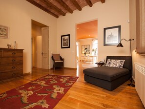 Una sala de estar acogedora con un sofá, un aparador de madera, un tapete floral rojo y un comedor al fondo.