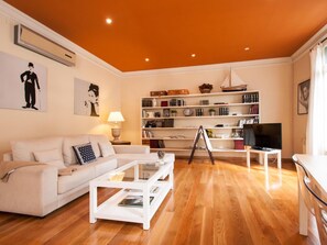 Una sala de estar con sofá, mesa de centro, estantería y televisor.