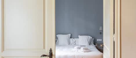Un dormitorio con cama, almohadas, una mesita de noche, lámpara y ventilador de techo.