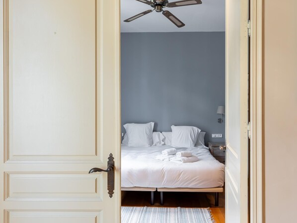 Une chambre à coucher avec un lit, des oreillers, une table de chevet, une lampe et un ventilateur de plafond.