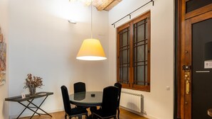 A dining area with a round table, four chairs, a hanging lamp, a window with wooden frames, and a door with a lock. - Apartamento Deluxe de dos Habitaciones (Barcelona)