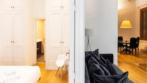 A hotel room with a bed, a white wardrobe, a desk with a chair, and a dining area with a table and chairs. - Apartamento Deluxe de dos Habitaciones (Barcelona)