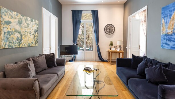 A living room with two sofas, a glass coffee table, a flat-screen TV, and a large window with curtains. - Apartamento Deluxe de dos Habitaciones (Barcelona)