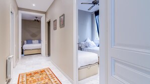 A hallway leading to a bedroom with a ceiling fan, a bed, and a nightstand.