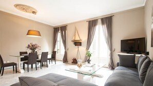 A modern living room with a sofa, dining table, chairs, and a TV.