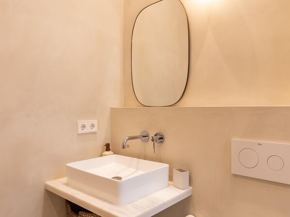 Une salle de bain avec un lavabo blanc, un miroir et un luminaire fixé au mur.