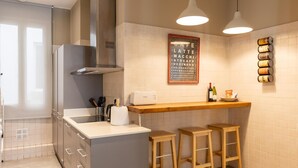 A modern kitchen with a central island, bar stools, a built-in oven, and a wall-mounted coffee machine.