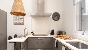 A modern kitchen with a stainless steel range hood, a wall clock, a hanging basket light, and a breakfast bar with a toaster and orange juice. - Apartamento Superior de Tres Dormitorios (Barcelona)