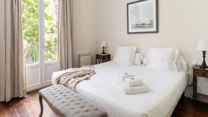 A hotel room with a large bed, a window with curtains, a bedside table with a lamp, and a framed picture on the wall. - Apartamento Superior de Tres Dormitorios (Barcelona)