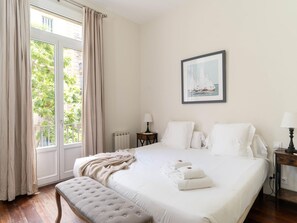 Een hotelkamer met een groot bed, een raam met gordijnen, een nachtkastje met een lamp en een lijst met een afbeelding aan de muur.