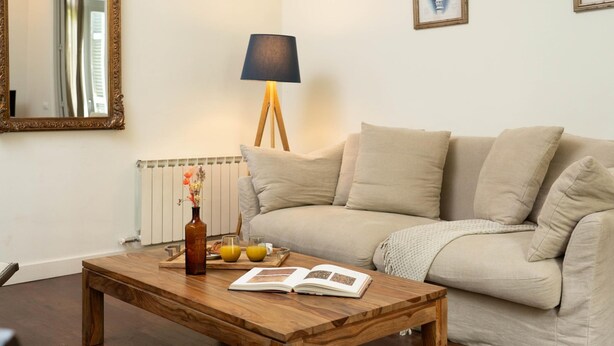 A living room with a wooden coffee table, a sofa, a floor lamp, a mirror, and framed pictures on the wall. - Apartamento Superior de Tres Dormitorios (Barcelona)