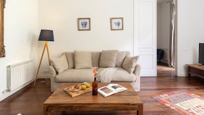 A living room with a sofa, coffee table, and a lamp. There are two framed pictures on the wall and a door leading to another room. - Apartamento Superior de Tres Dormitorios (Barcelona)