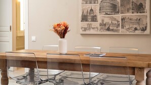 A dining table with a clear glass top, a white vase with dried flowers, and a yellow pendant light.