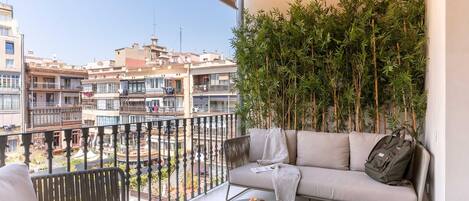 A balcony with a sofa, a small table with croissants, and a view of buildings and a pool.