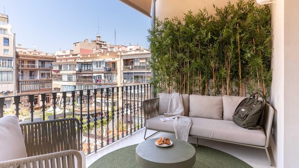A balcony with a sofa, a small table with croissants, and a view of buildings and a pool.