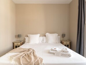 Una habitación de hotel con una cama, dos mesitas de noche, una lámpara, una pila de toallas y una colcha.