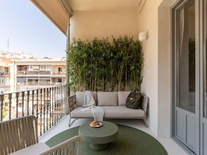 A balcony with a sofa, a round table with a plate of food, and a green rug. - Apto Superior de Tres Habitaciones con Terraza (Barcelona)