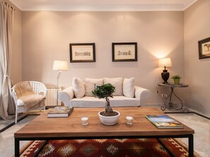 A living room with a sofa, a coffee table, a chair, and two framed pictures on the wall. - Apto Superior de Tres Habitaciones con Terraza (Barcelona)