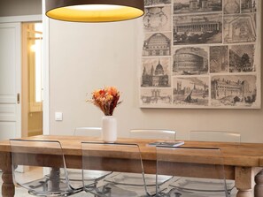 A dining table with a clear glass top, a white vase with dried flowers, and a yellow pendant light. - Apto Superior de Tres Habitaciones con Terraza (Barcelona)