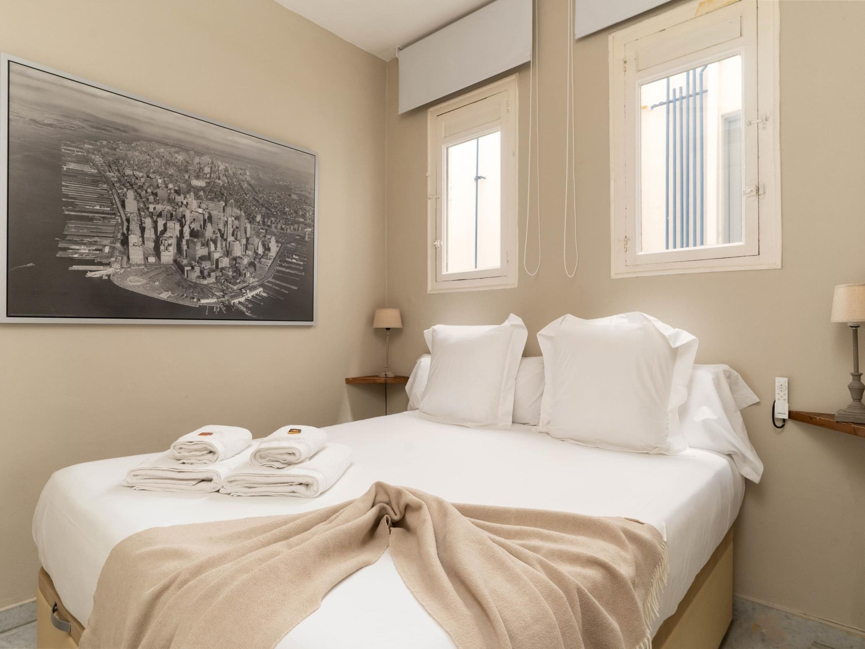 Hotelkamer met een bed, een groot stadsfotografie, twee ramen, een nachtkastje en een lamp.