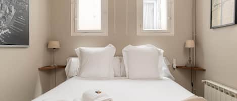 A hotel room with a bed, two bedside tables with lamps, a window, and a framed picture on the wall.