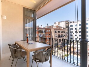 Un balcón con mesa y sillas, un jarrón con flores y vistas a edificios.