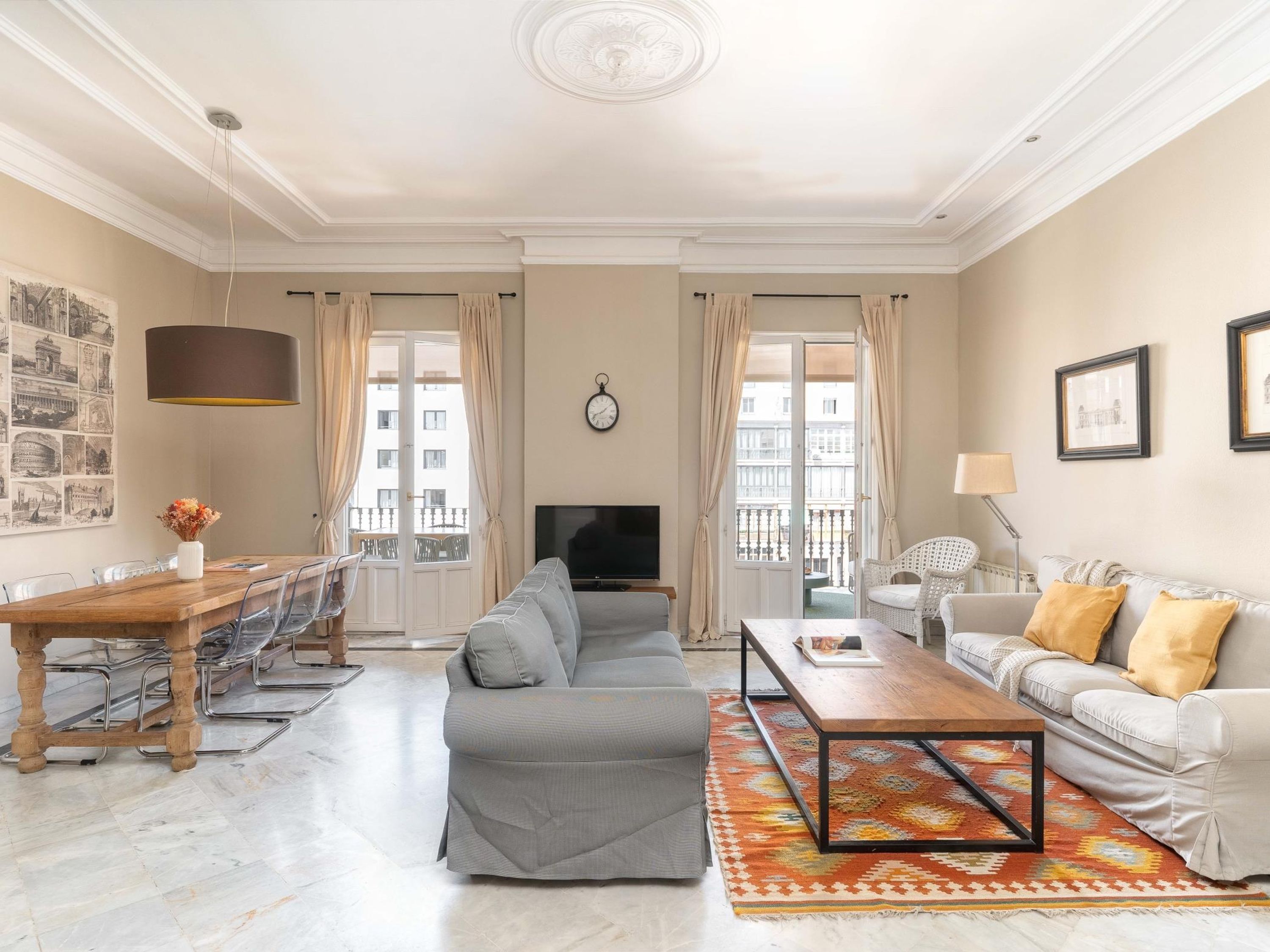 A living room with a sofa, a coffee table, a TV, a dining table with chairs, and a patterned rug.