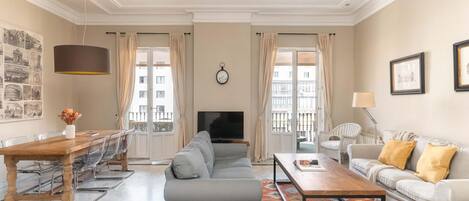 A living room with a sofa, a coffee table, a TV, a dining table with chairs, and a patterned rug.