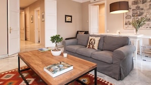 A modern living room with a grey sofa, a wooden coffee table with a magazine, a small potted plant, and a large lamp.